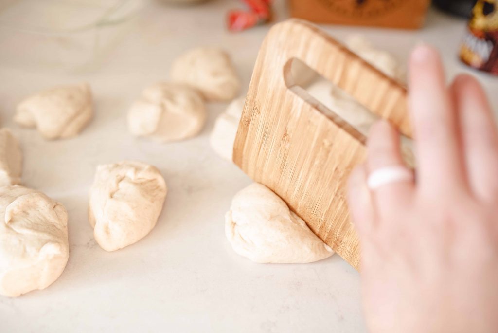 a hand cutting sourdough flatbread dough with a bamboo bench scraper