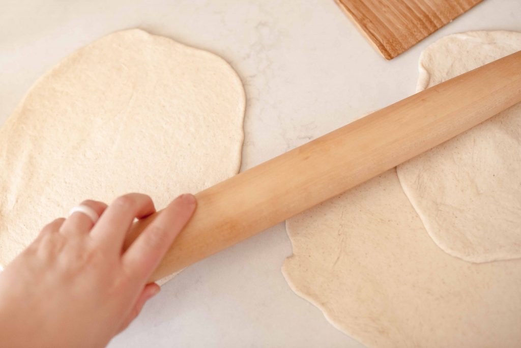 a hand rolling out sourdough flatbread dough with a wooden rolling pin
