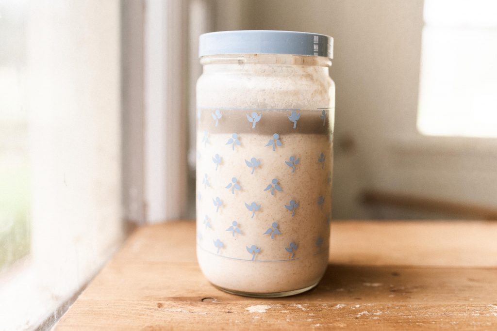an antique blue floral jar with inactive sourdough starter next to a window