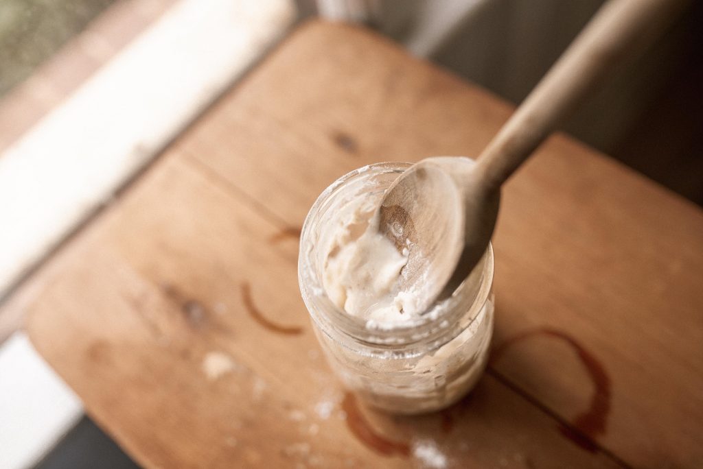 a glass jar of sourdough starter with a wooden spoon on a wooden counter