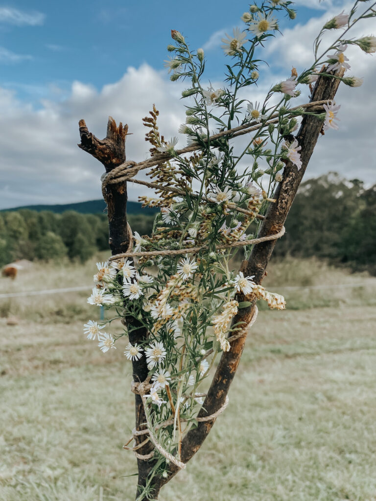 a nature weave stick with foliage and wildflowers with the view of the mountains and pasture behind
