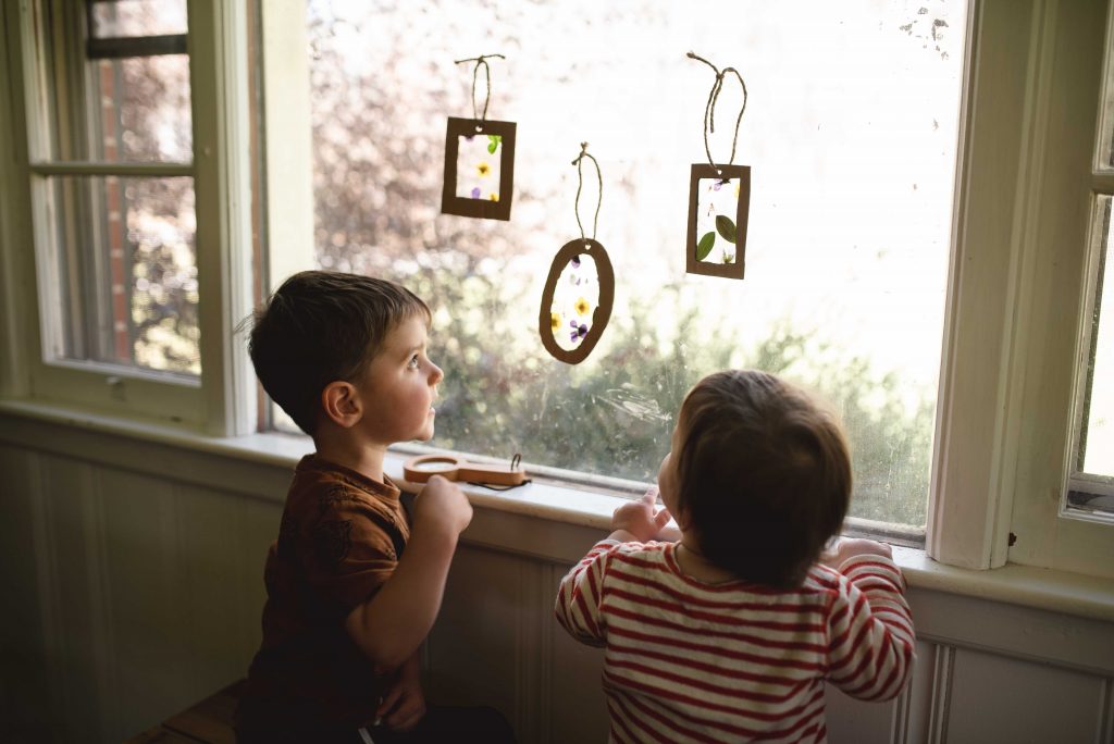two children looking up at three sun catchers hanging in the window