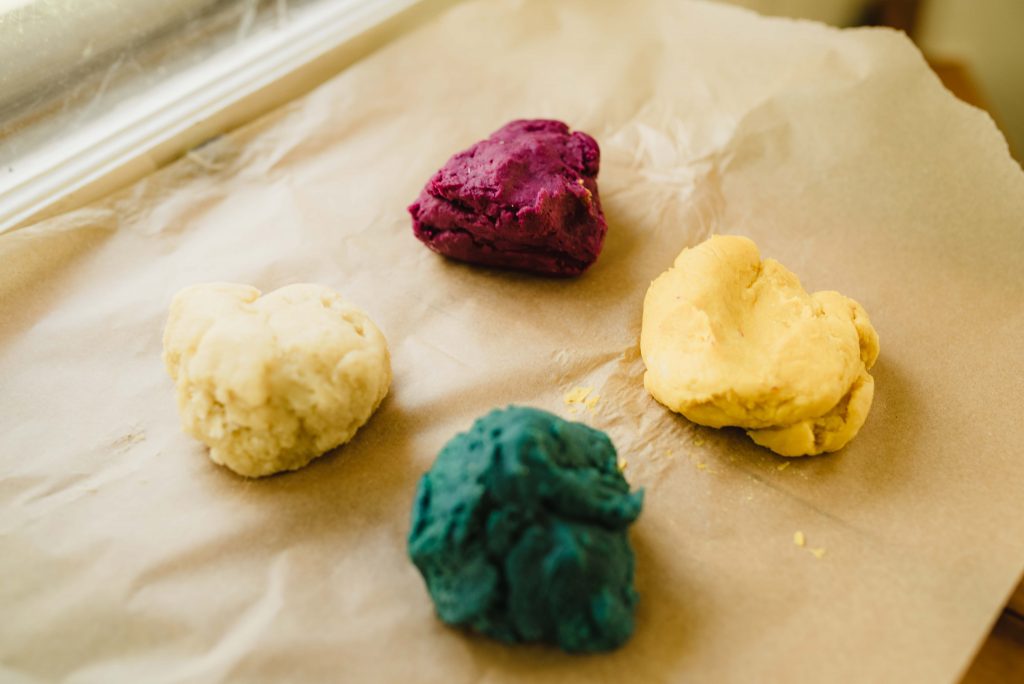 a sheet of wax paper with four colors of vegetable dyed playdough