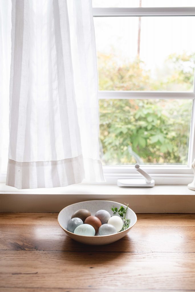 a bowl of vegetable dyed easter eggs under a farmhouse kitchen window