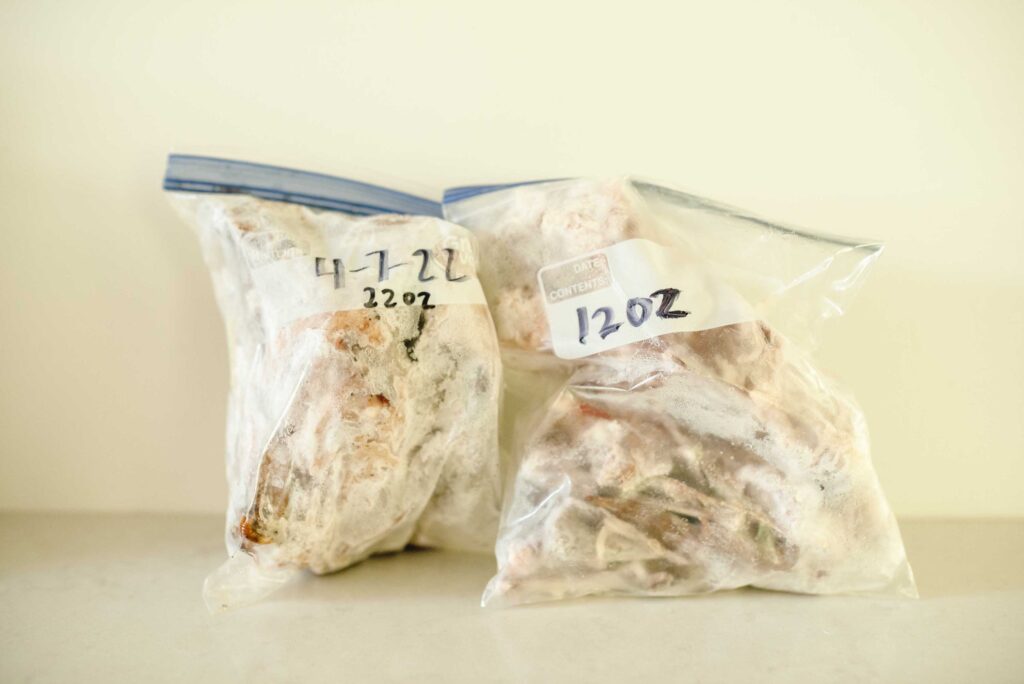ziplock bags on a marble counter containing chicken bones and date/weight written on the bag